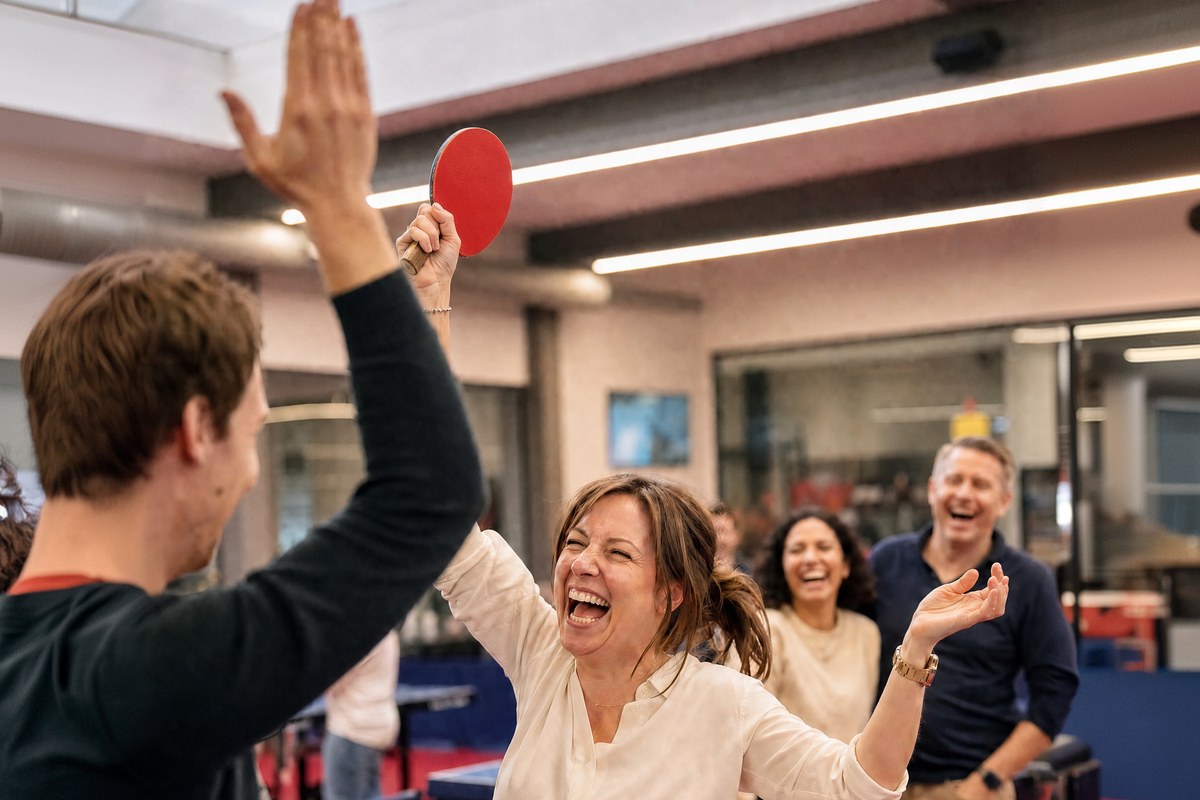 Twee collega's geven elkaar een high five aan de tafel, de rest van het team lacht mee